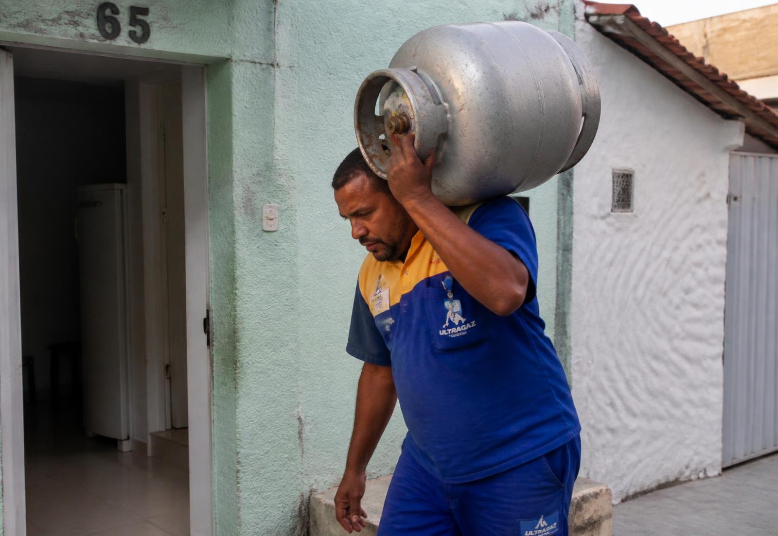 Entregador do Bibi Gás carregando botijão de gás em frente a uma residência em Palhoça